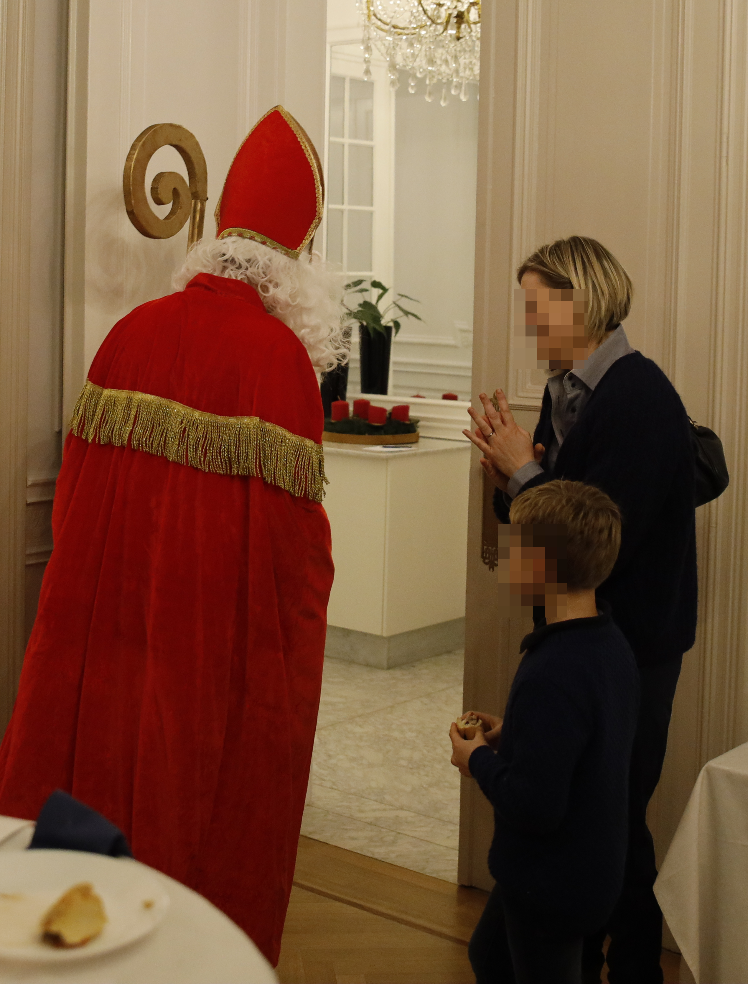 Frau mit gefalteten Händen verabschiedet Nikolaus, der durch die große Türe aus dem Saal schreitet