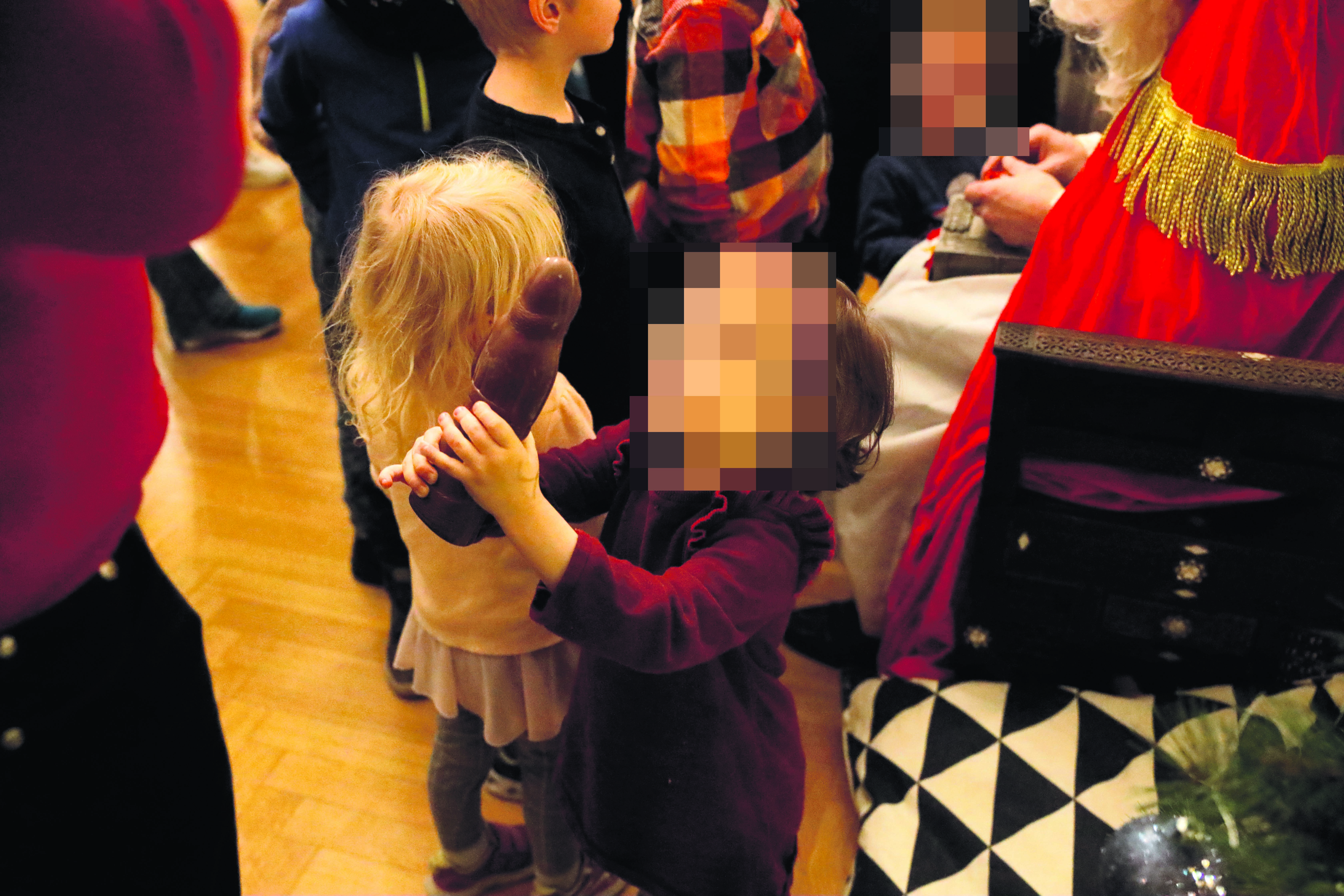 ca. dreijähriges Mädchen (Gesicht verpixelt) hält den ausgepackten besonders braunen CSU-Schokoladennikolaus freudestrahlend vor sich.
