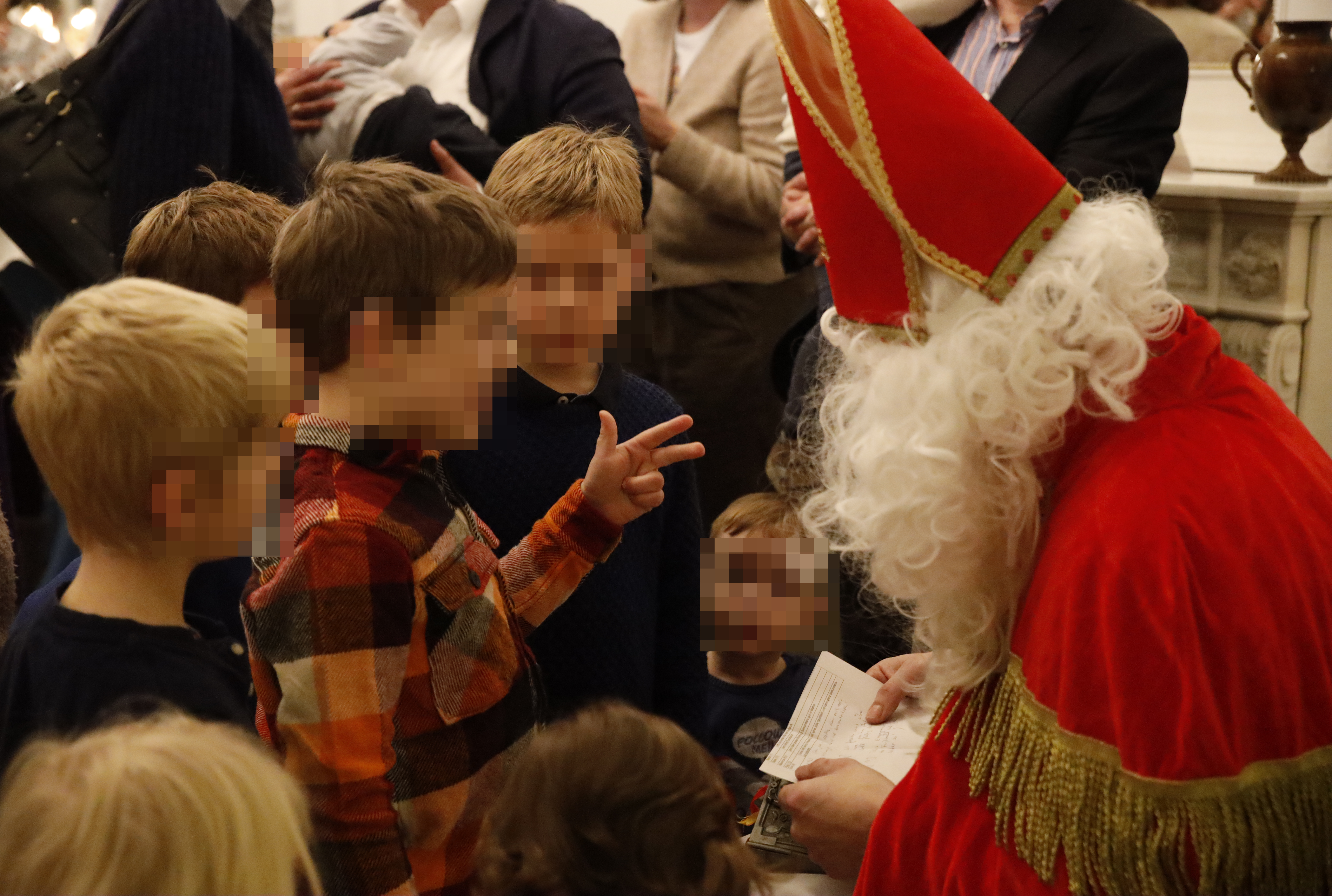 Kinder stehen dicht vor Nikolaus. Ein Junge hält drei Finger hoch.